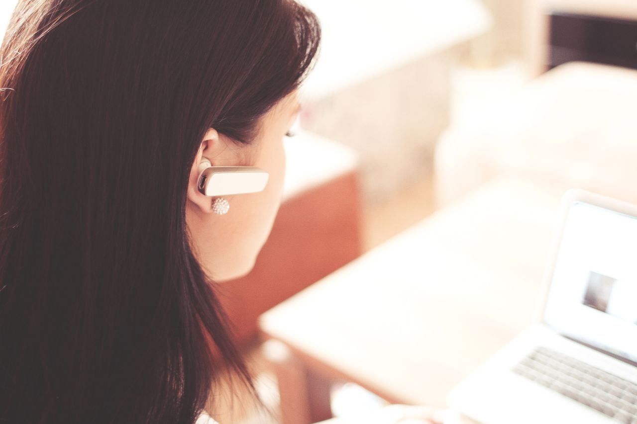services-04 A businesswoman using a Bluetooth headset while working on her laptop in a modern office.